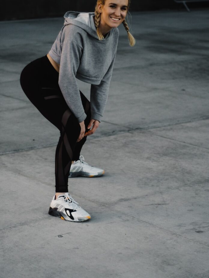 Photo by Charles Etoroma woman in gray long sleeve shirt and black leggings sitting on gray concrete floor